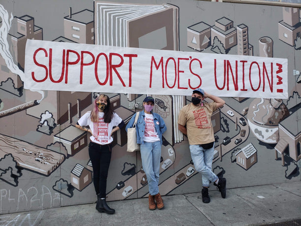 Moe's Books workers (left to right) Phoebe Wong, Kalie McGuirl, and Sam Sax stand in front of a banner at their April 2021 rally.