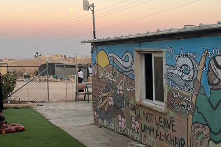 An image of a mural in the Palestinian village of Umm al Khair. The mural shoes a Shepard in a Keffiyah on the hills of the village, with a Mahmoud Darwish quote and the declaration "we will not leave Umm al-Khair"