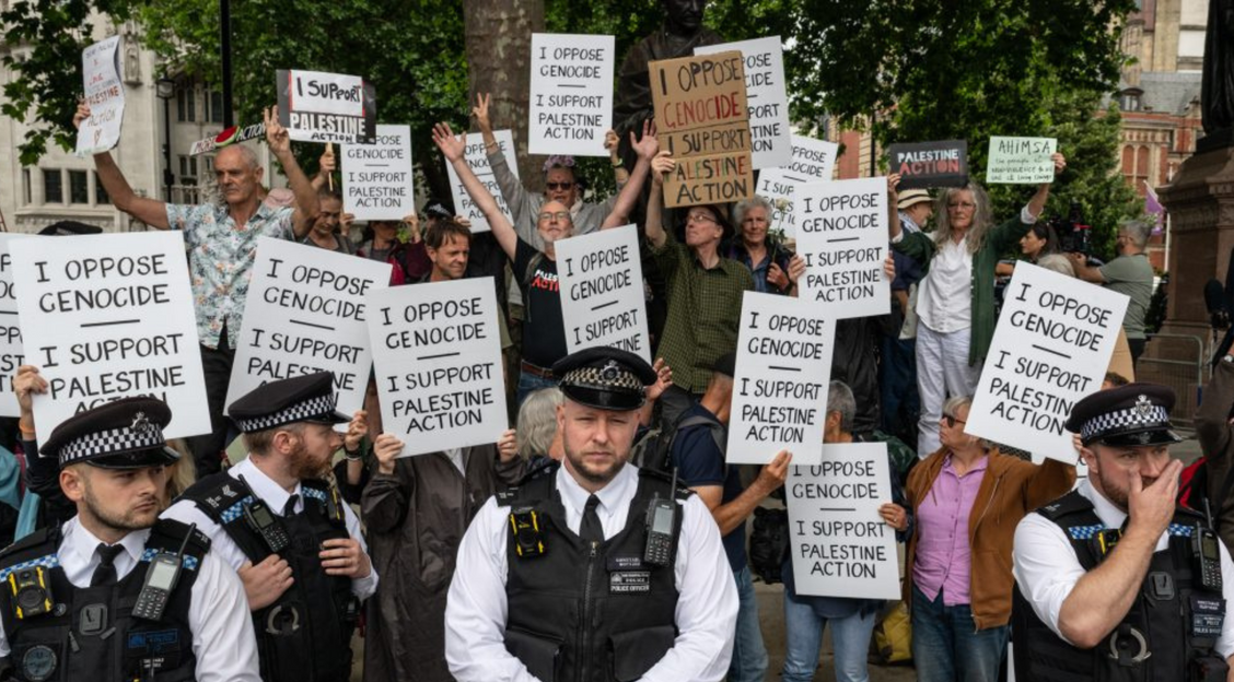 a group of Defend Our Juries demonstrators hold signs behind a row of police officers in London