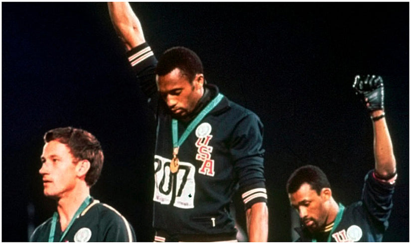 Tommie Smith (center) and John Carlos raise their fists in solidarity on the podium at the '68 Olympics. via Angelo Cozzi